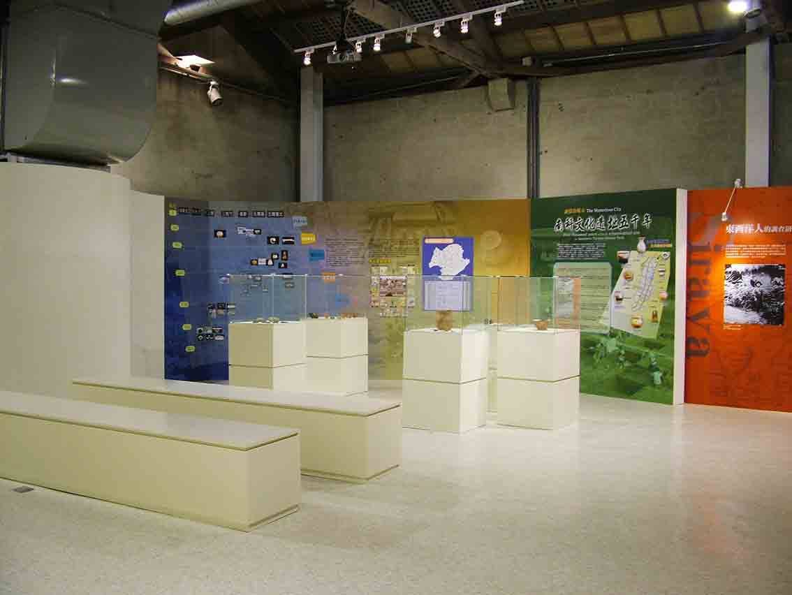 展場全景，藍黃綠橘四色分區展牆與玻璃展櫃陣列