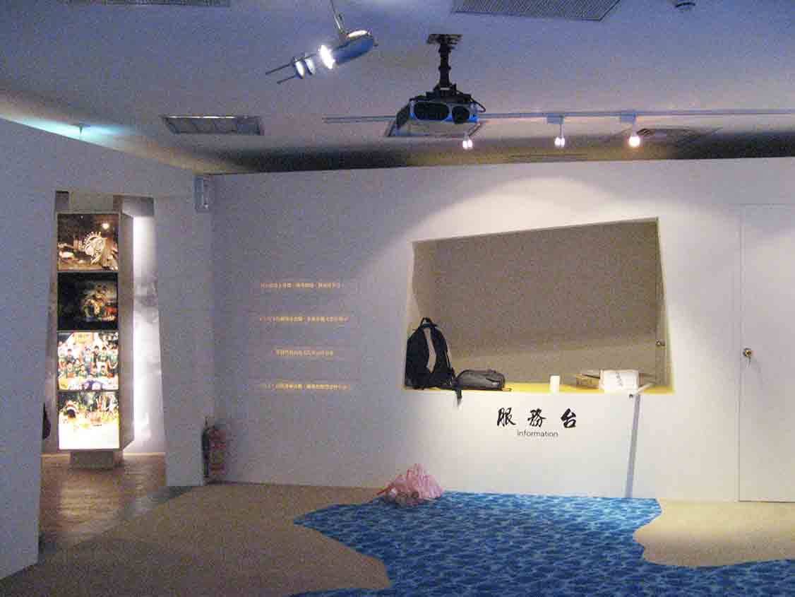 烈嶼鄉史館服務台區，水藍地坪、投影機與燈箱柱形塑入口意象