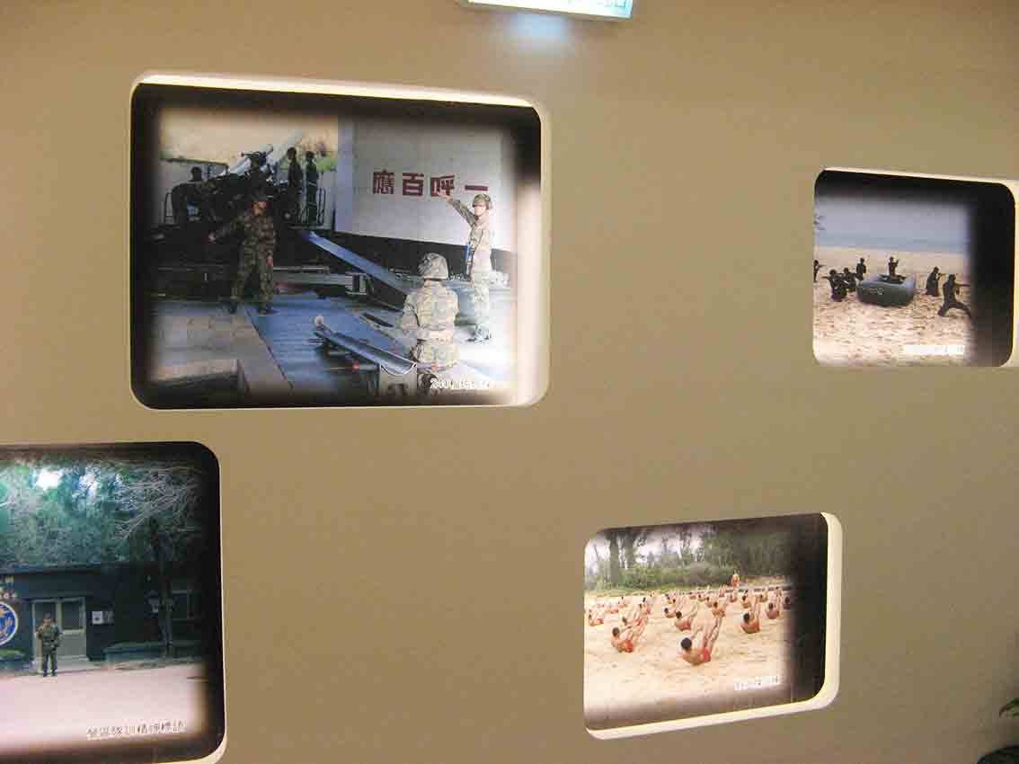 湖井頭戰史館橄欖綠牆面圓角窗格陣列，呈現「一呼百應」標語下的砲兵操演、橡皮艇登陸與沙灘體能訓練等彩色實景照