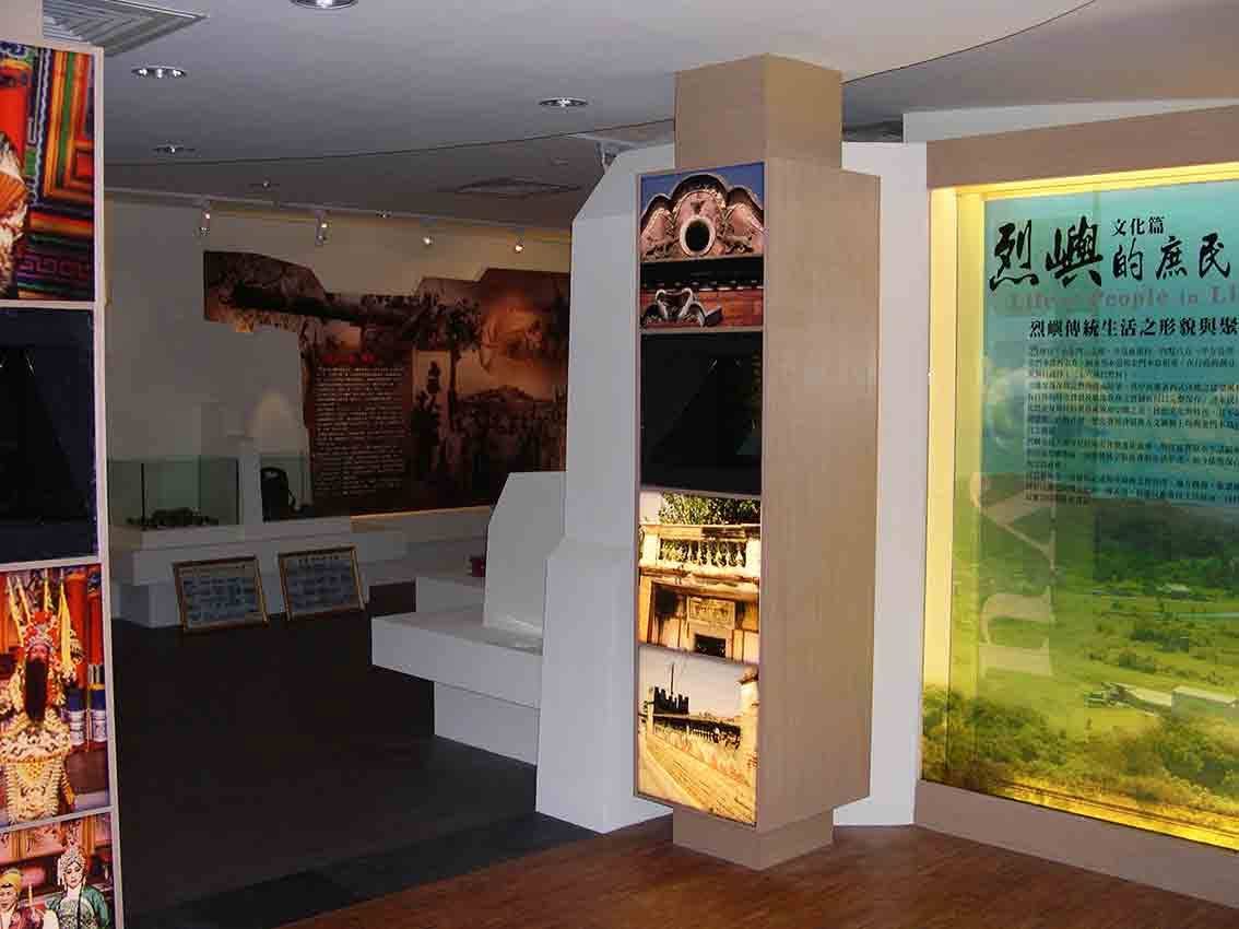 烈嶼鄉史館文化篇展區轉角，老建築剪影燈箱柱串連庶民生活展板與綠色聚落空拍燈箱