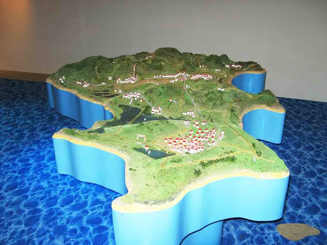 烈嶼鄉史館立體地形模型俯視，小金門綠地、聚落與道路精密呈現，外圍藍色海面地坪烘托離島意象