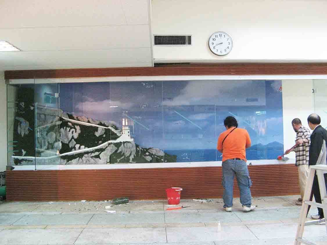 烈嶼鄉史館大圖玻璃輸出施工現場，工班正在組裝海岸燈塔場景的玻璃壁畫