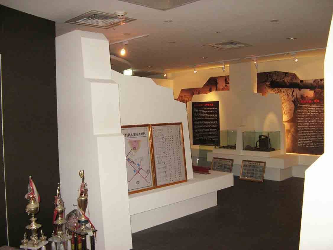 烈嶼鄉史館戰役展區白色碉堡造型量體，前方陳列獎盃、地圖與名冊文件