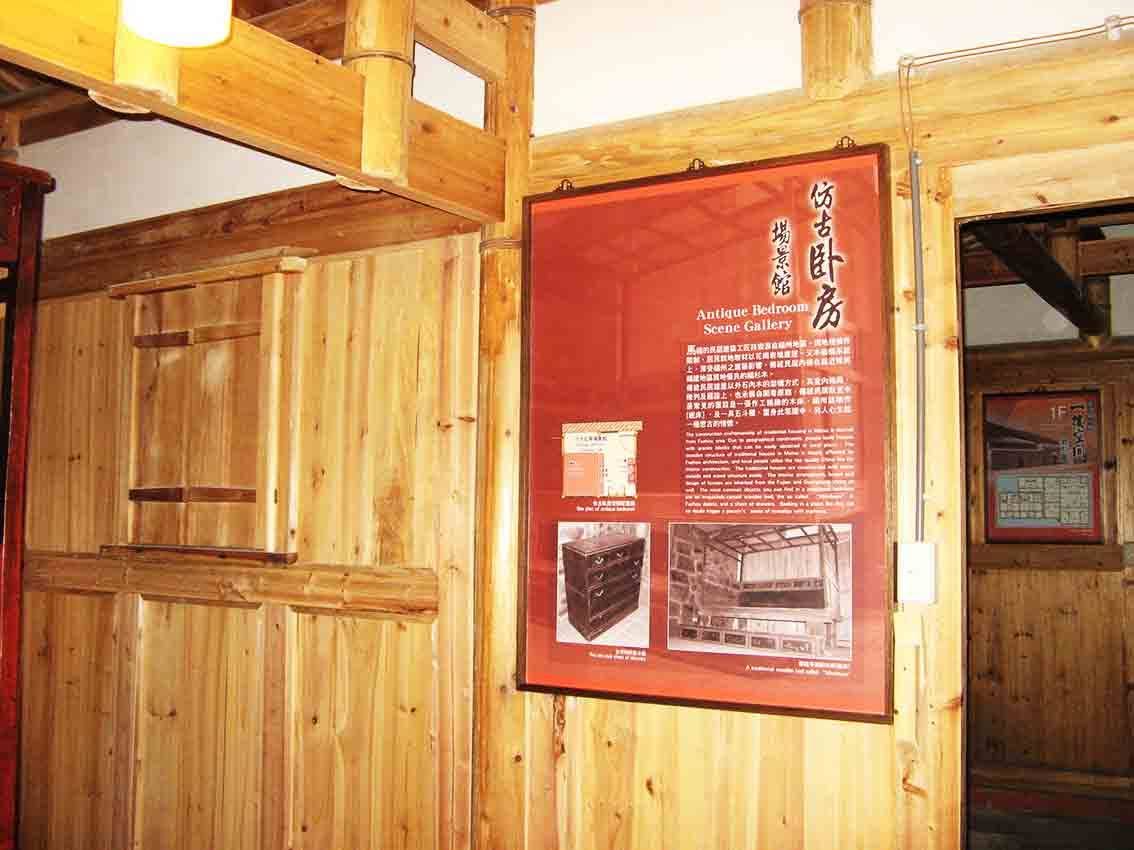 馬祖后里文物館仿古臥房場景館全景，木構板牆與展示櫃前懸掛紅色「仿古臥房 Antique Bedroom Scene Gallery」海報