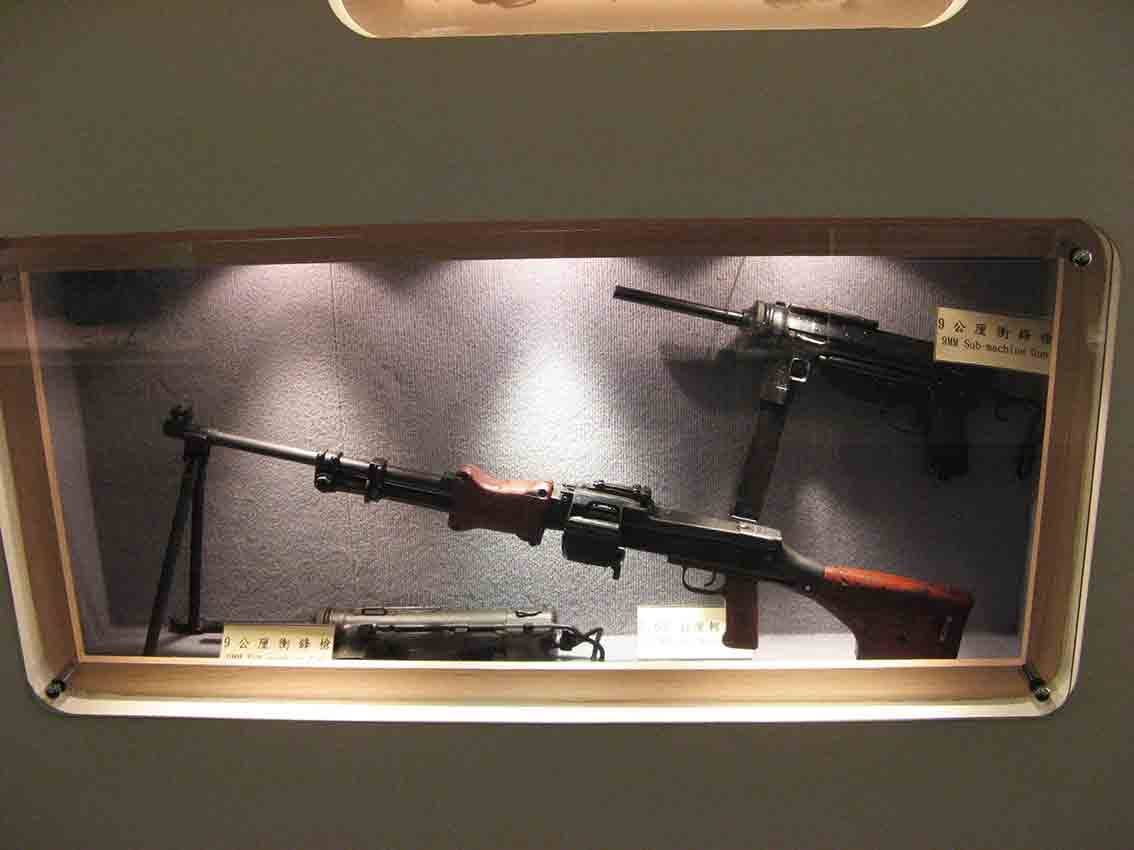 湖井頭戰史館木框玻璃展示櫃內陳列「9公厘衝鋒槍 9MM Sub-machine Gun」與帶兩腳架的輕機槍特寫