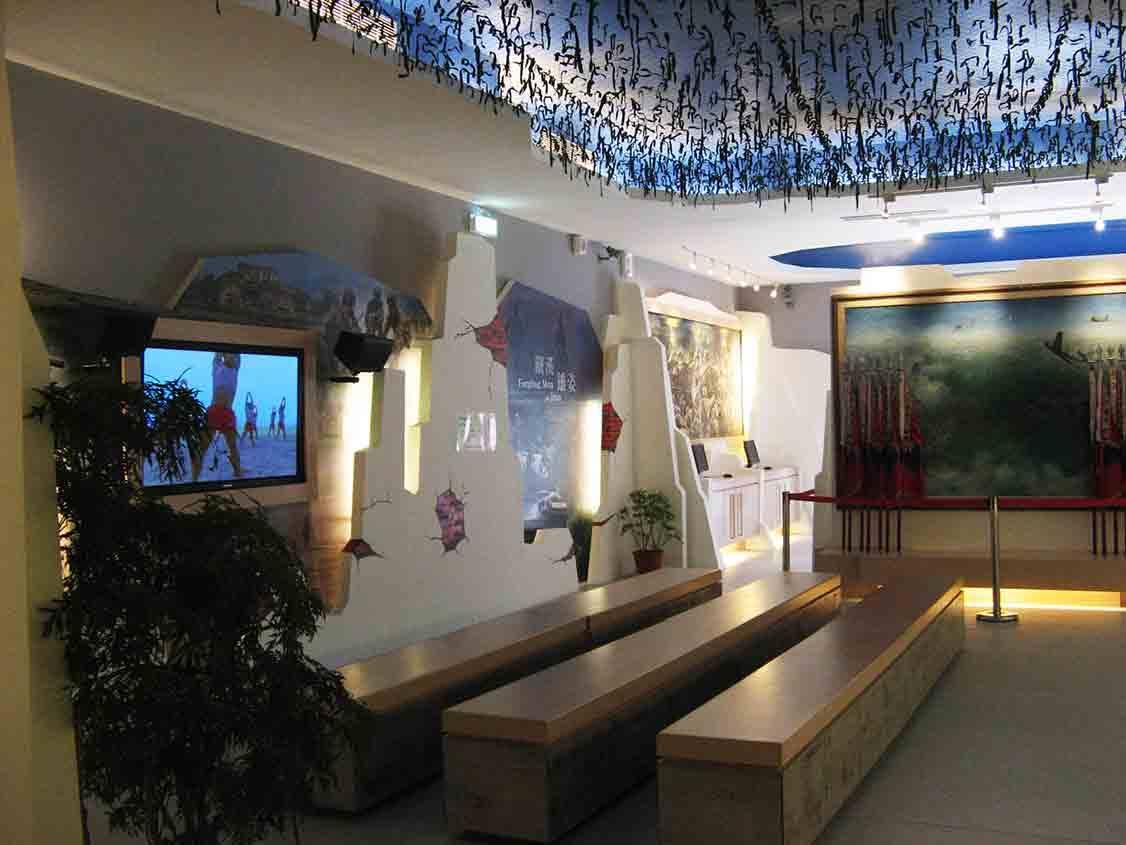 湖井頭戰史館多媒體影音休憩區，藍底書法天花板下設置液晶電視、「鐵漢雄姿」直立輸出、油畫與木紋階梯座椅
