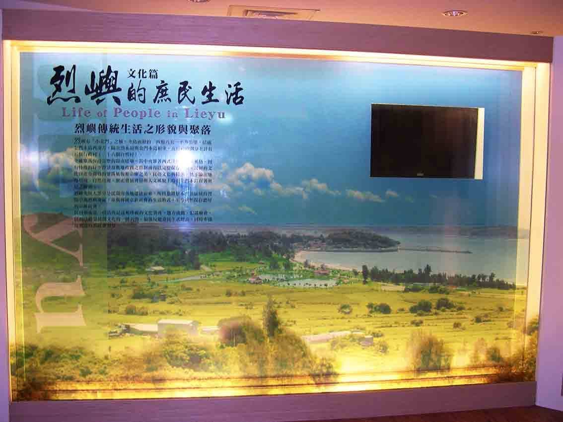 烈嶼鄉史館「烈嶼的庶民生活」文化篇展板，大圖以小金門海岸聚落空拍為背景並嵌入影像播放螢幕