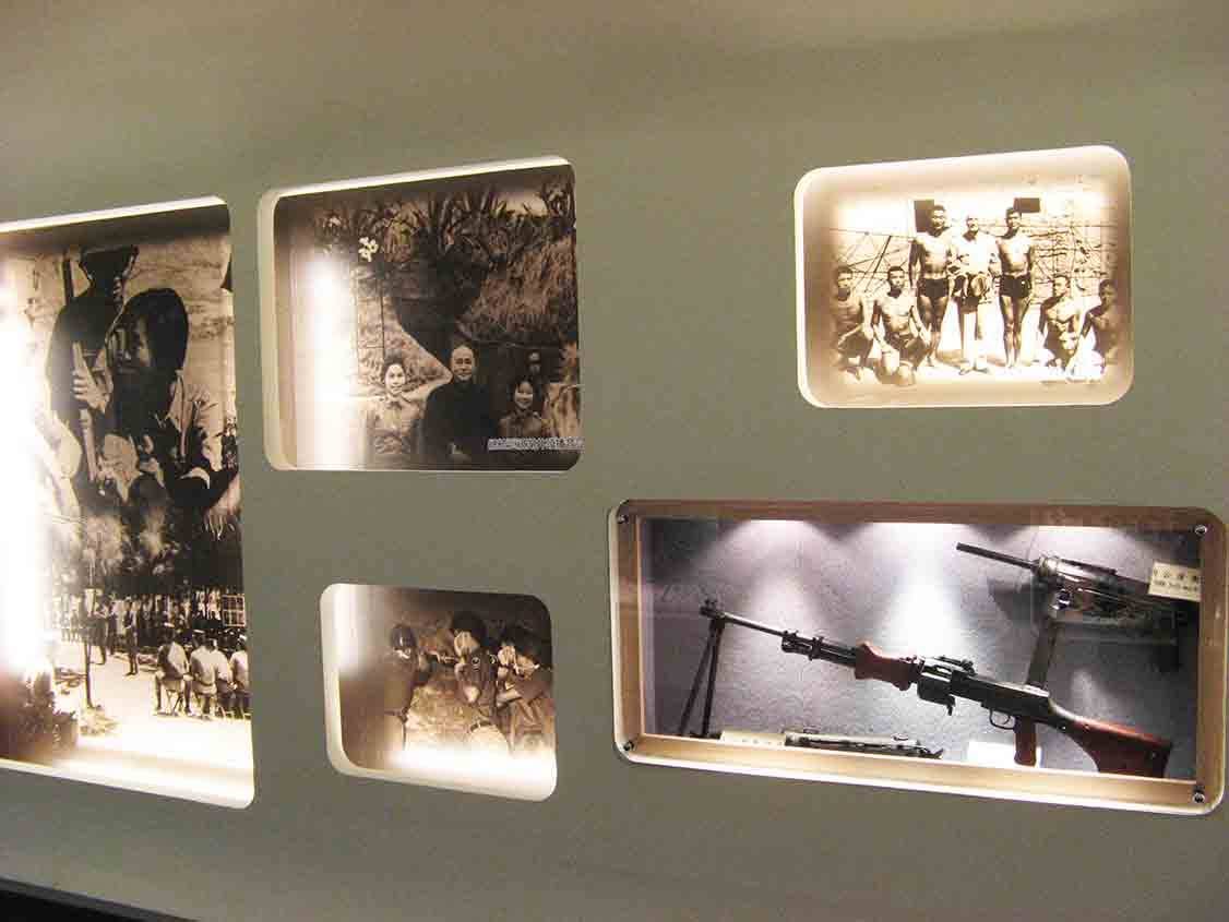 湖井頭戰史館嵌牆圓角窗格展牆，呈現挑擔擔水、蔣公伉儷視察、戰俘合影與木框內的機槍實體展示