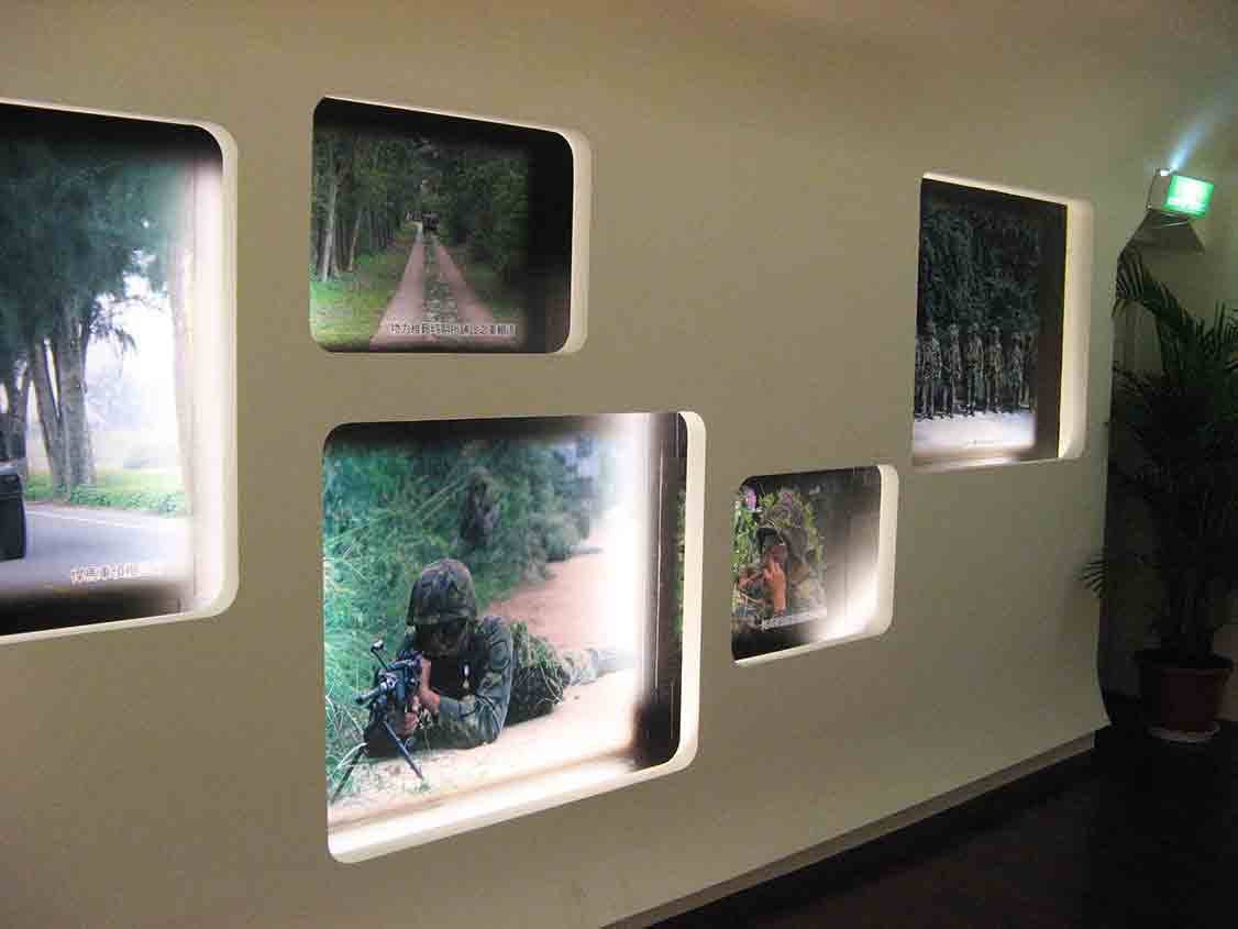 湖井頭戰史館橄欖綠牆面圓角燈箱群，呈現木麻黃林道、偽裝部隊潛伏與狙擊兵叢林匍匐射擊等彩色實景照