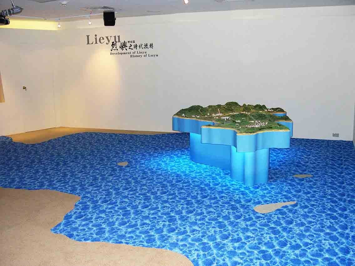 烈嶼鄉史館「烈嶼之時代流轉 Development of Lieyu / History of Lieyu」歷史篇展區，藍色海面地坪上立體小金門地形模型