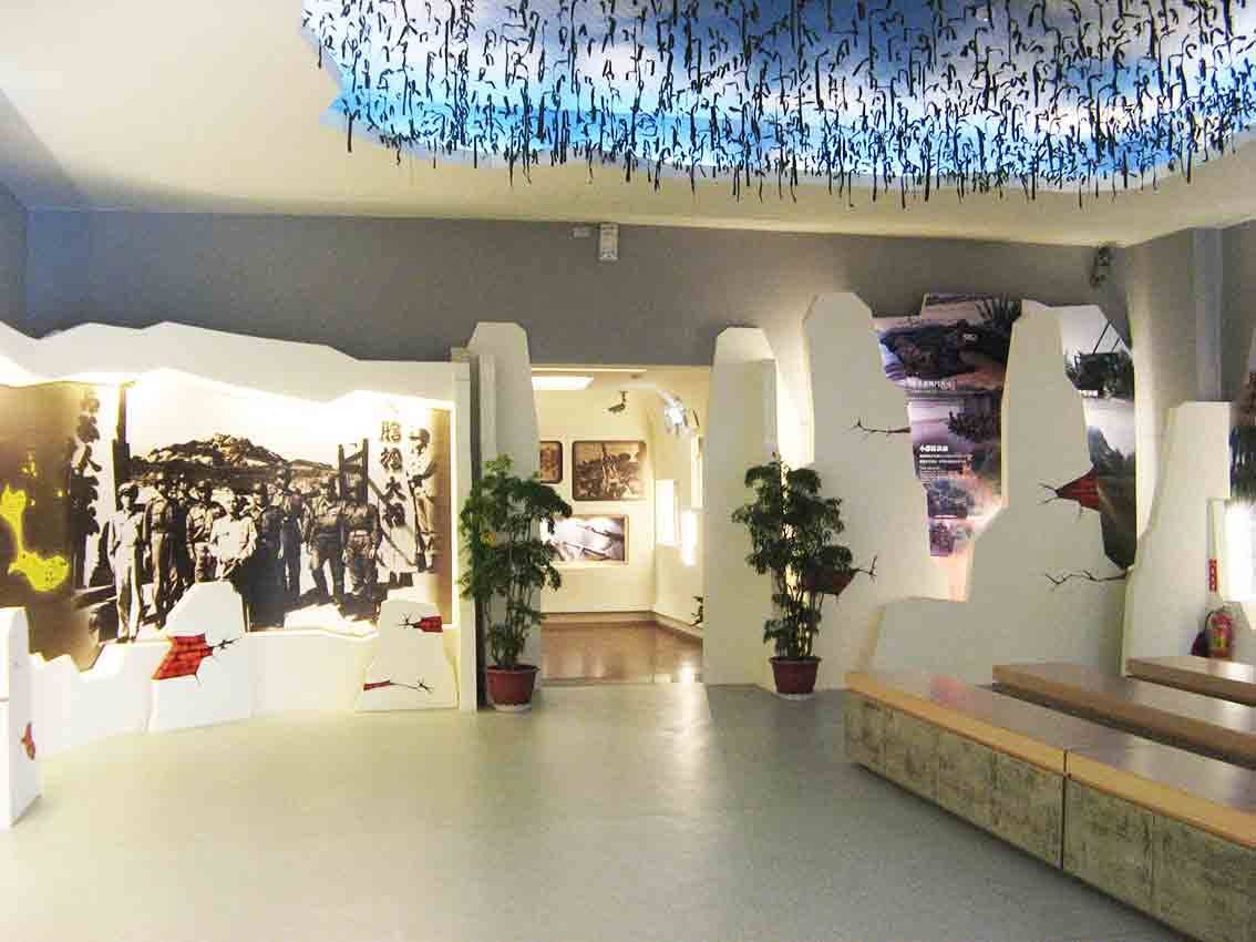 烈嶼鄉史館戰事展廳全景，天花懸吊藍底墨書帷幕與兩側碉堡輪廓造型牆面圍塑出戰地氛圍