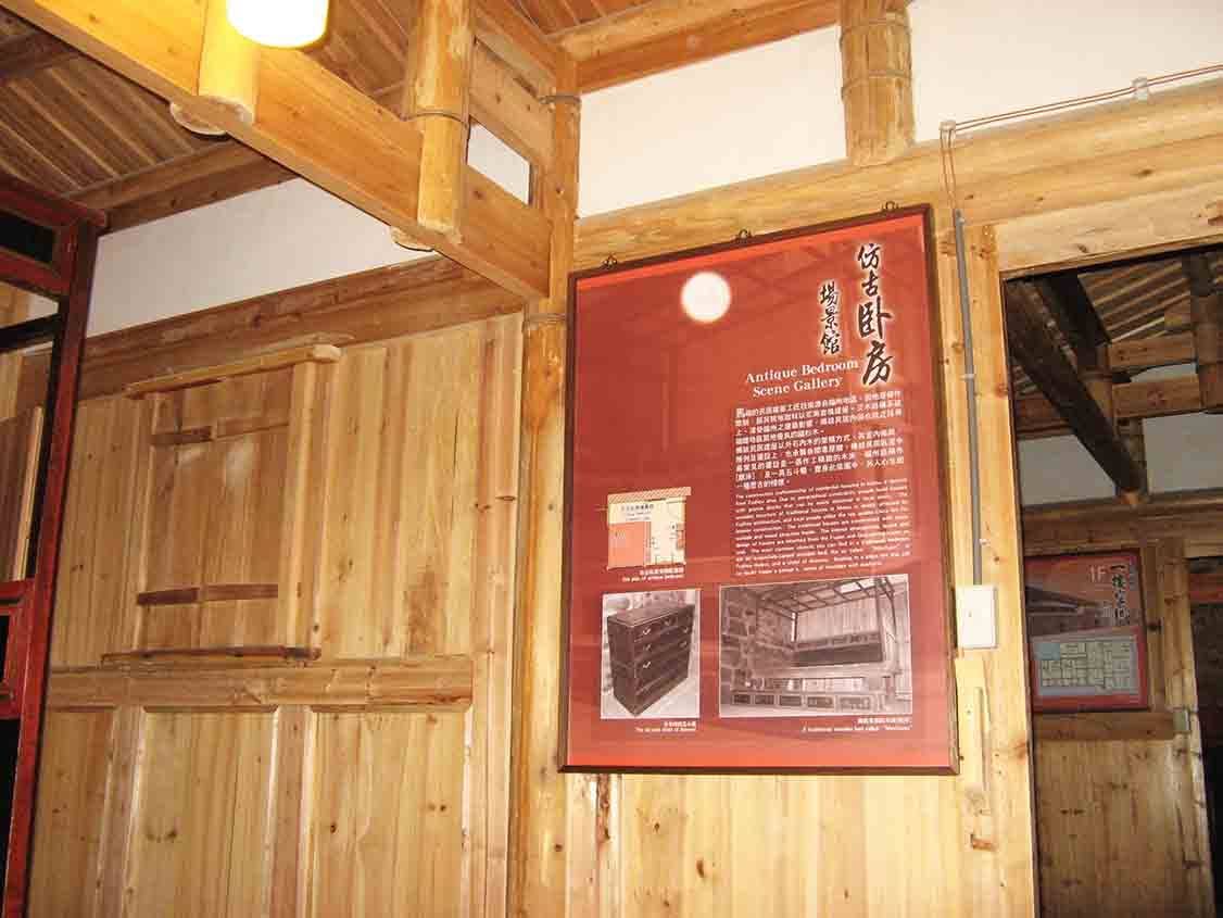 馬祖后里文物館仿古臥房場景館展板，紅色解說海報懸掛於閩東木構板牆，搭配上層竹編窗櫺與木桁架