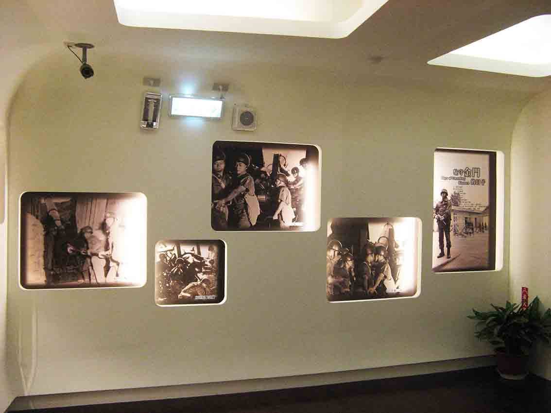 湖井頭戰史館圓拱坑道造型展廳，米白牆面嵌入五幅黑白戰地照片，記錄國軍砲兵操作、坑道作戰與「死守金門」海報