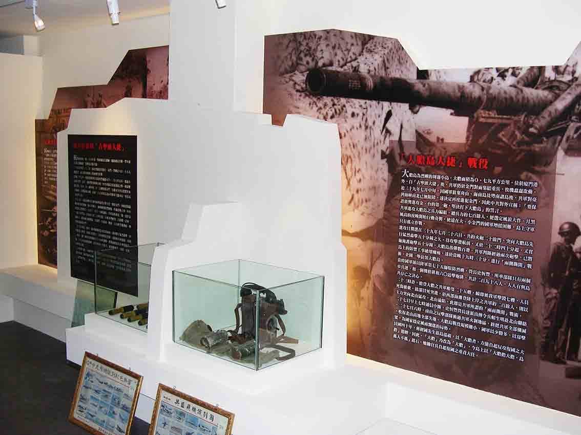 烈嶼鄉史館大膽島大捷戰役展區特寫，展示櫃陳列軍用器物並對應火砲大圖牆