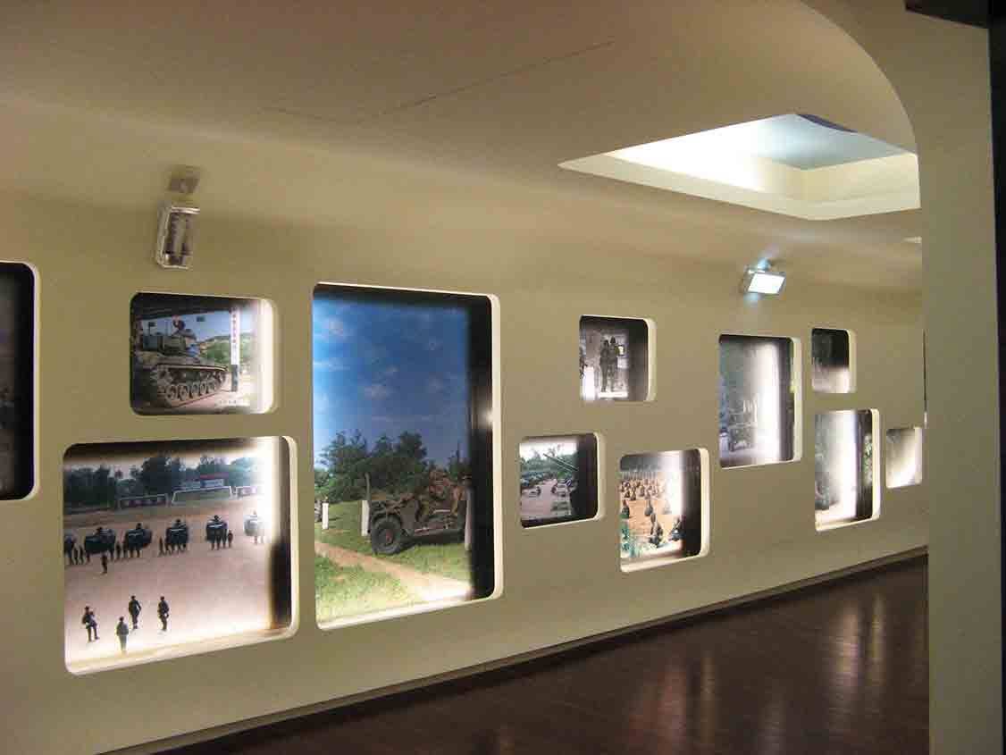 湖井頭戰史館弧形展廊圓角窗格陣列，呈現戰車陣列、吉普車、部隊集結與營區門口等彩色軍事實景照