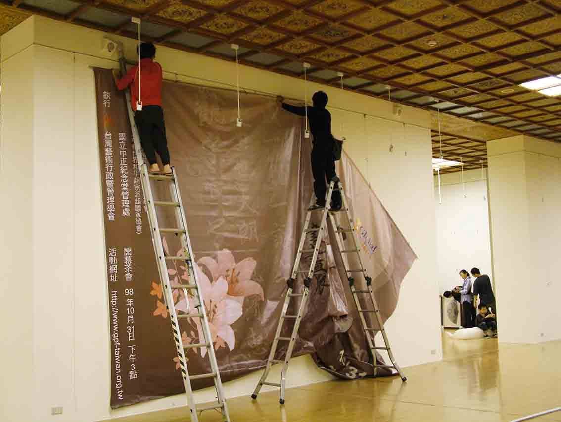 和平書畫展大圖施工——人員攀爬鋁梯張掛大圖布幕
