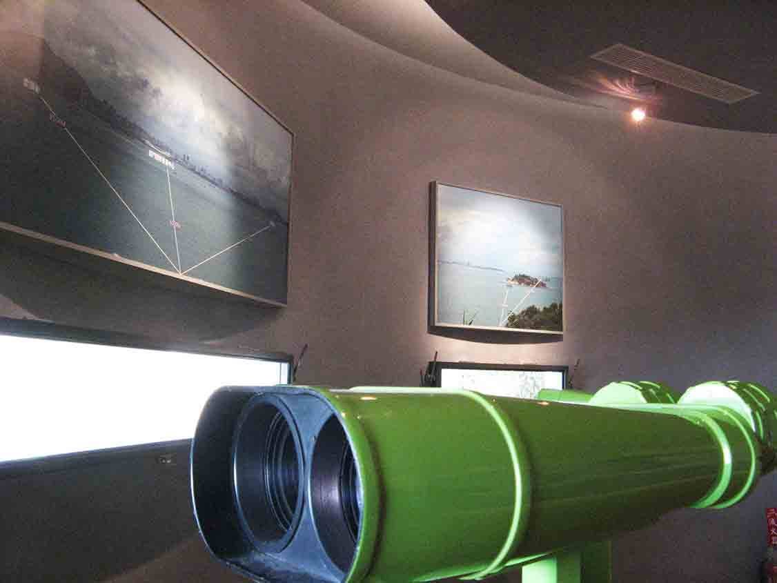 湖井頭戰史館瞭望觀測展區，綠色雙筒巨型望遠鏡指向觀景窗，牆上掛有對岸島嶼識別大圖與小型海景照片