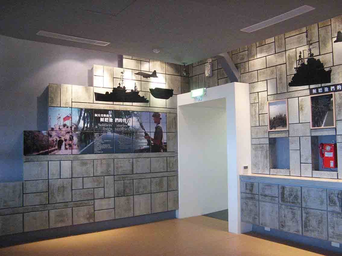 湖井頭戰史館「阿兵哥的故事 Soldiers' listen to their stories」主題展牆，水泥磚紋背景配軍艦剪影與紅色野戰電話