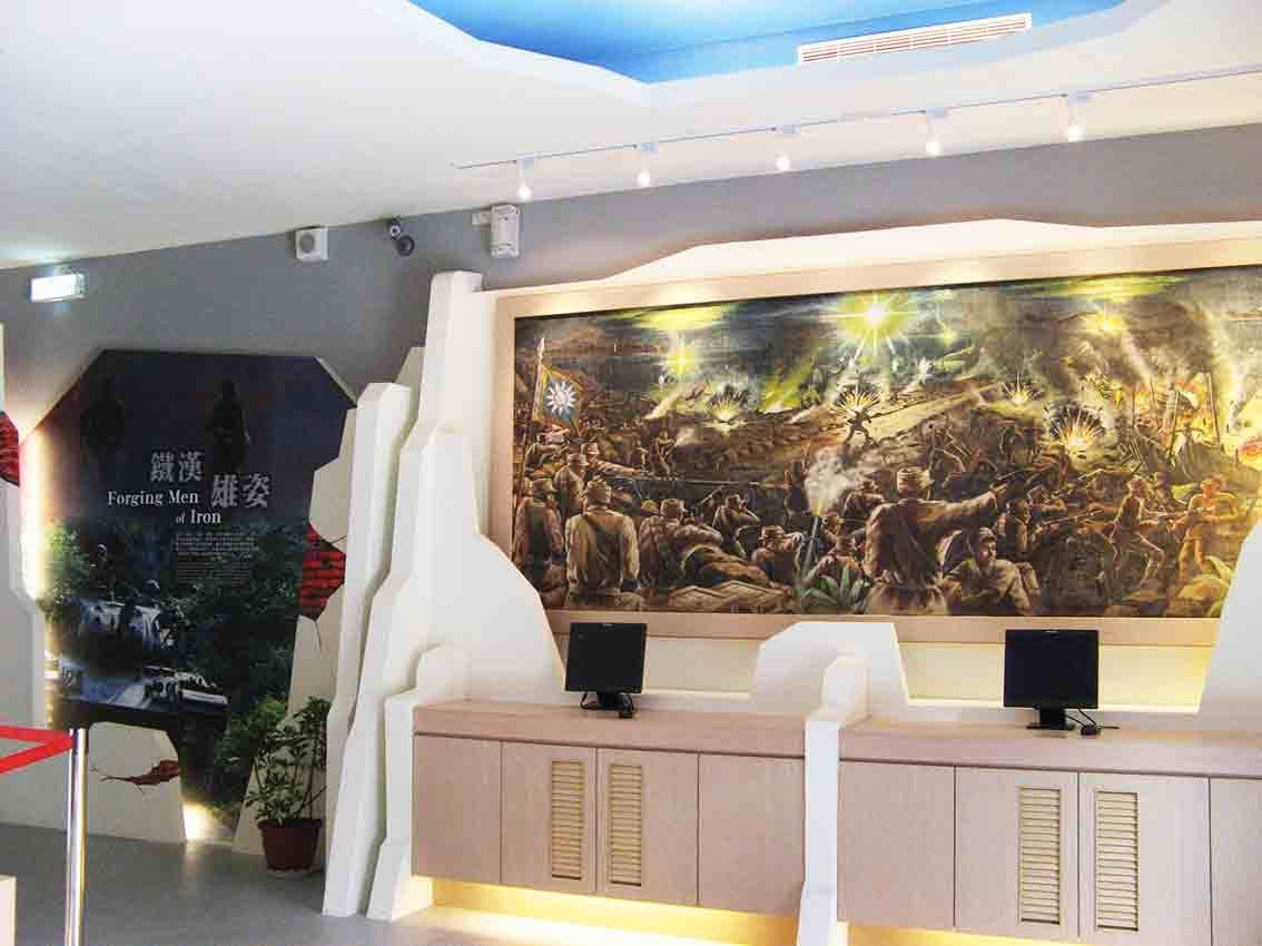 湖井頭戰史館「鐵漢雄姿 Forging Men of Iron」主題展區，巨幅國軍奮戰油畫搭配青天白日旗、白色山形造型牆與雙電視影音設備