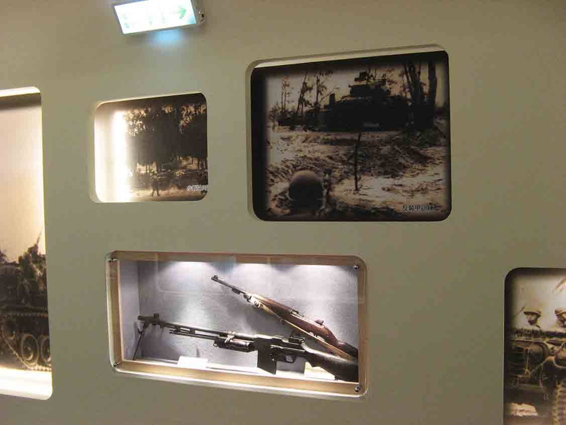 湖井頭戰史館牆面展示反裝甲訓練黑白舊照與下方壓克力框內的機槍、步槍實體展示