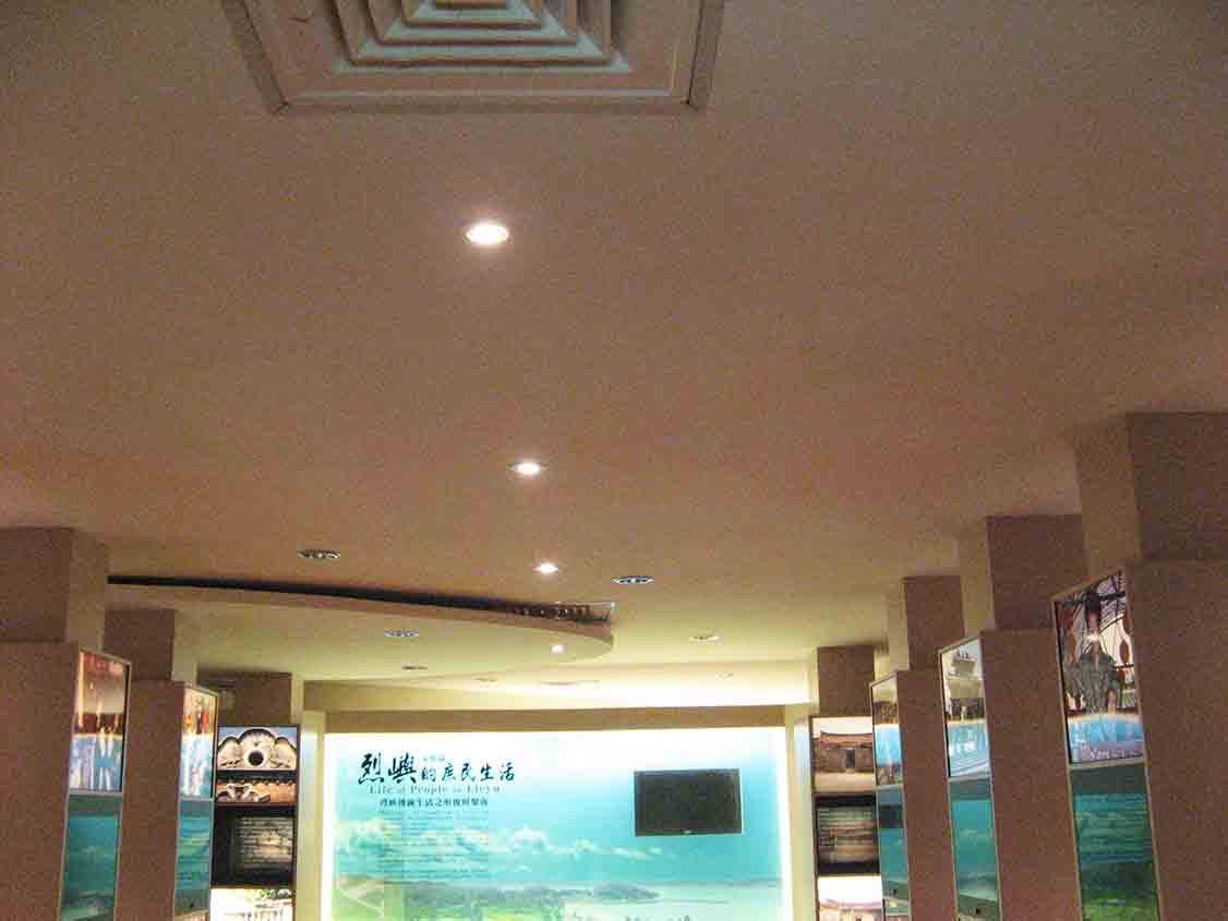 烈嶼鄉史館庶民生活主展區仰視，方格藻井天花、弧形吊頂與兩側發光展示柱所構成的展廳