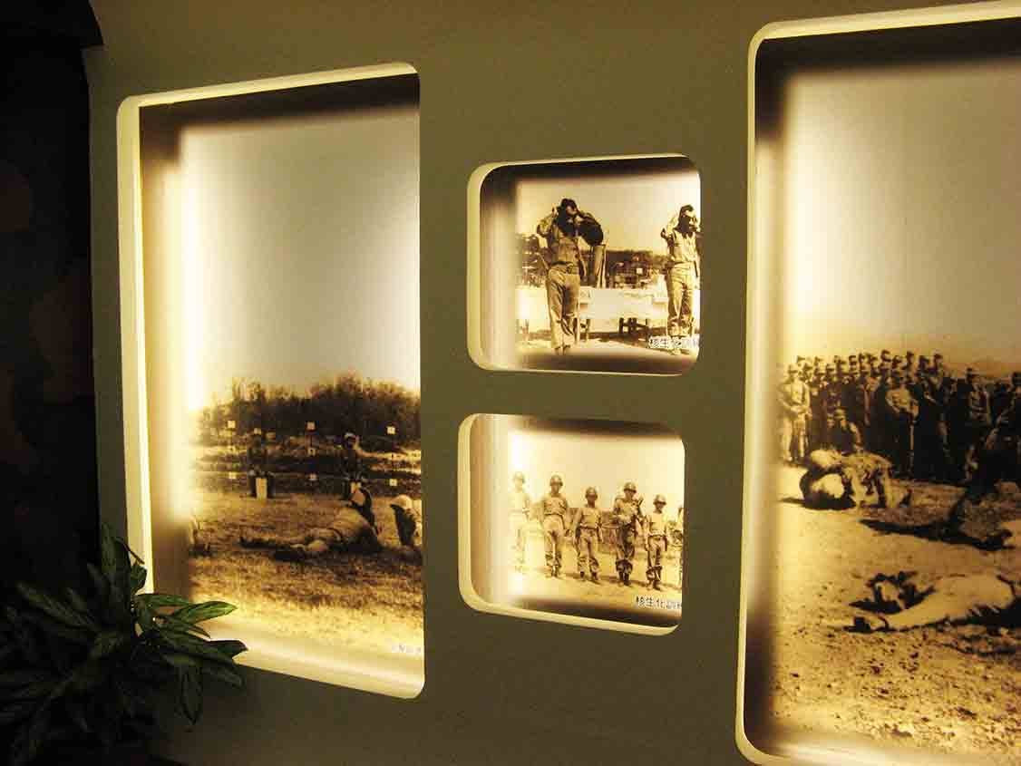湖井頭戰史館圓角窗格展牆，棕色調黑白照片呈現核生化防護演練、戰俘押解與部隊集結等歷史場景