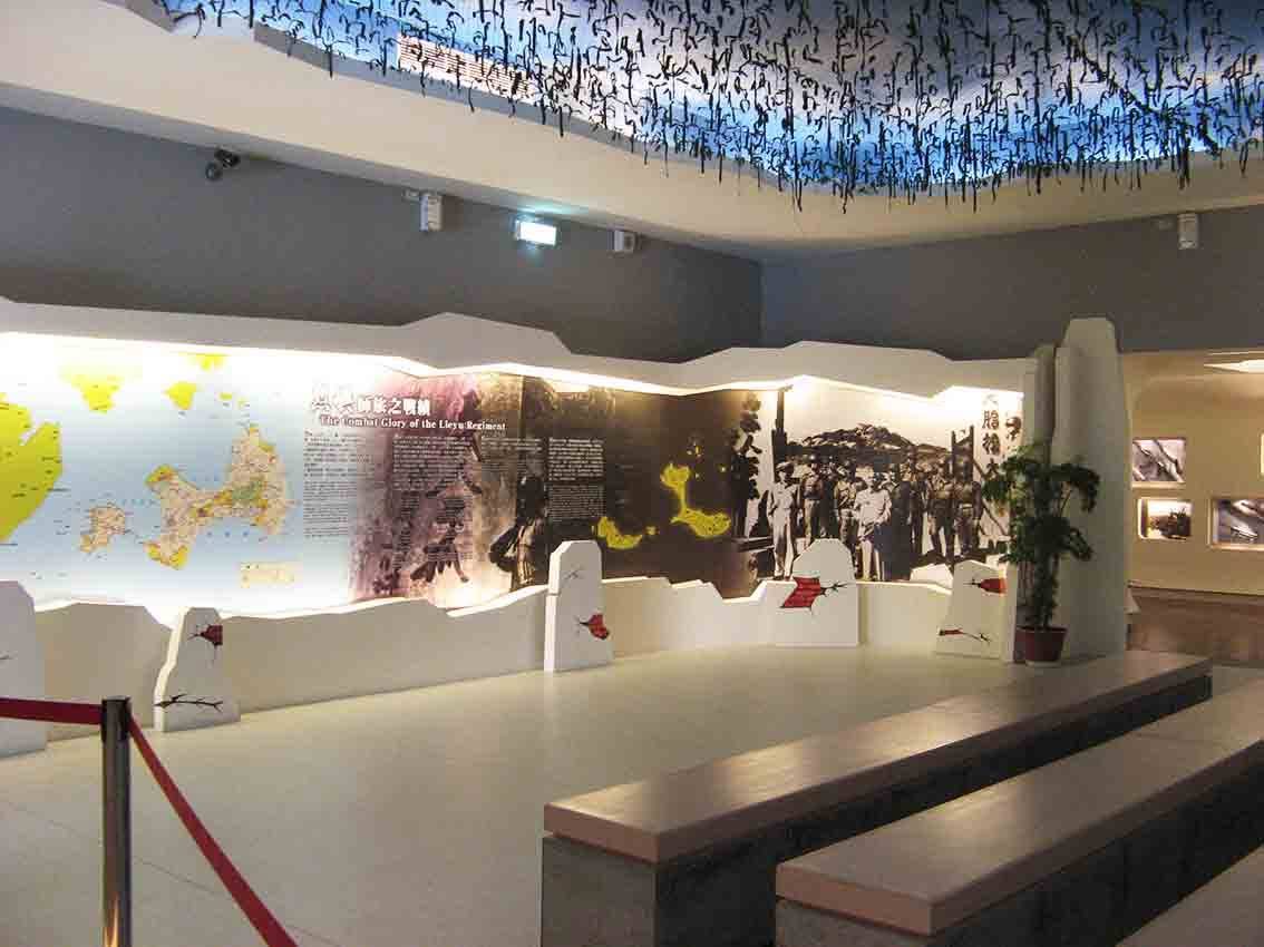 湖井頭戰史館「烈嶼師旅之戰績 The Combat Glory of the Lieyu Regiment」主題大型展牆全景，融合金門地圖、史料文字、戰地剪影與藍底書法天花板